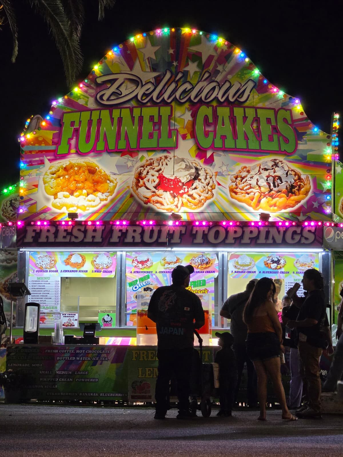 Delicious Funnel Cakes stand with neon lights and queue